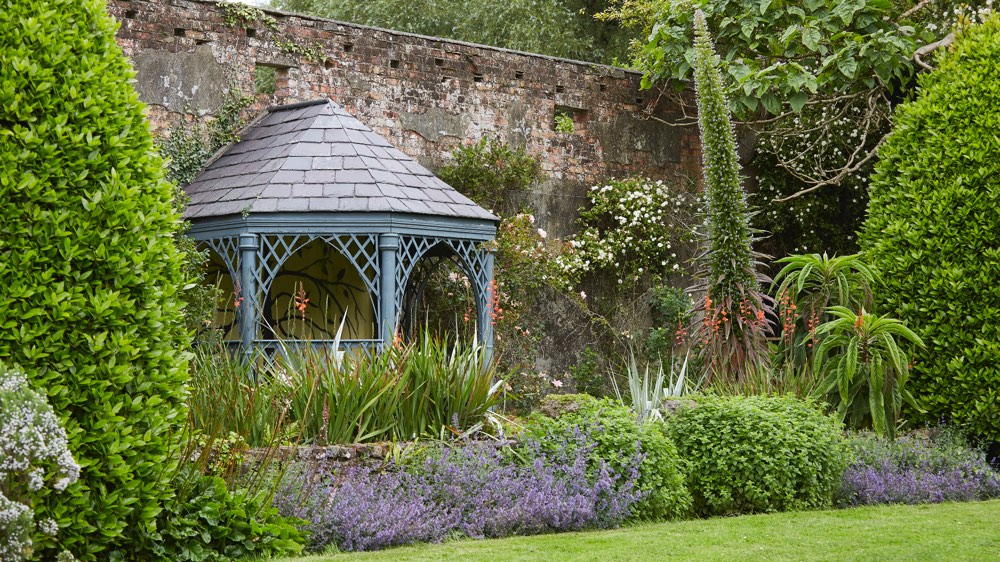 Wooden gazebo resting against a red brick wall at Seaforde Gardens